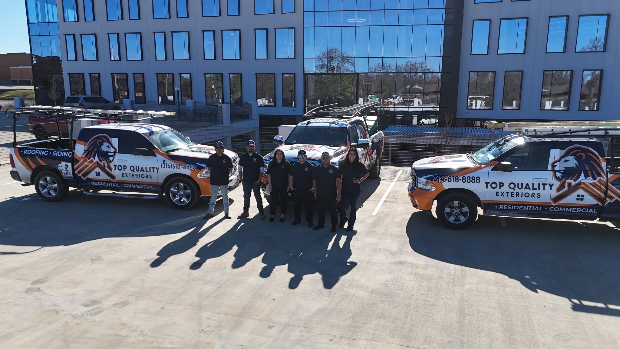 Top Quality Exteriors team standing beside three branded company trucks